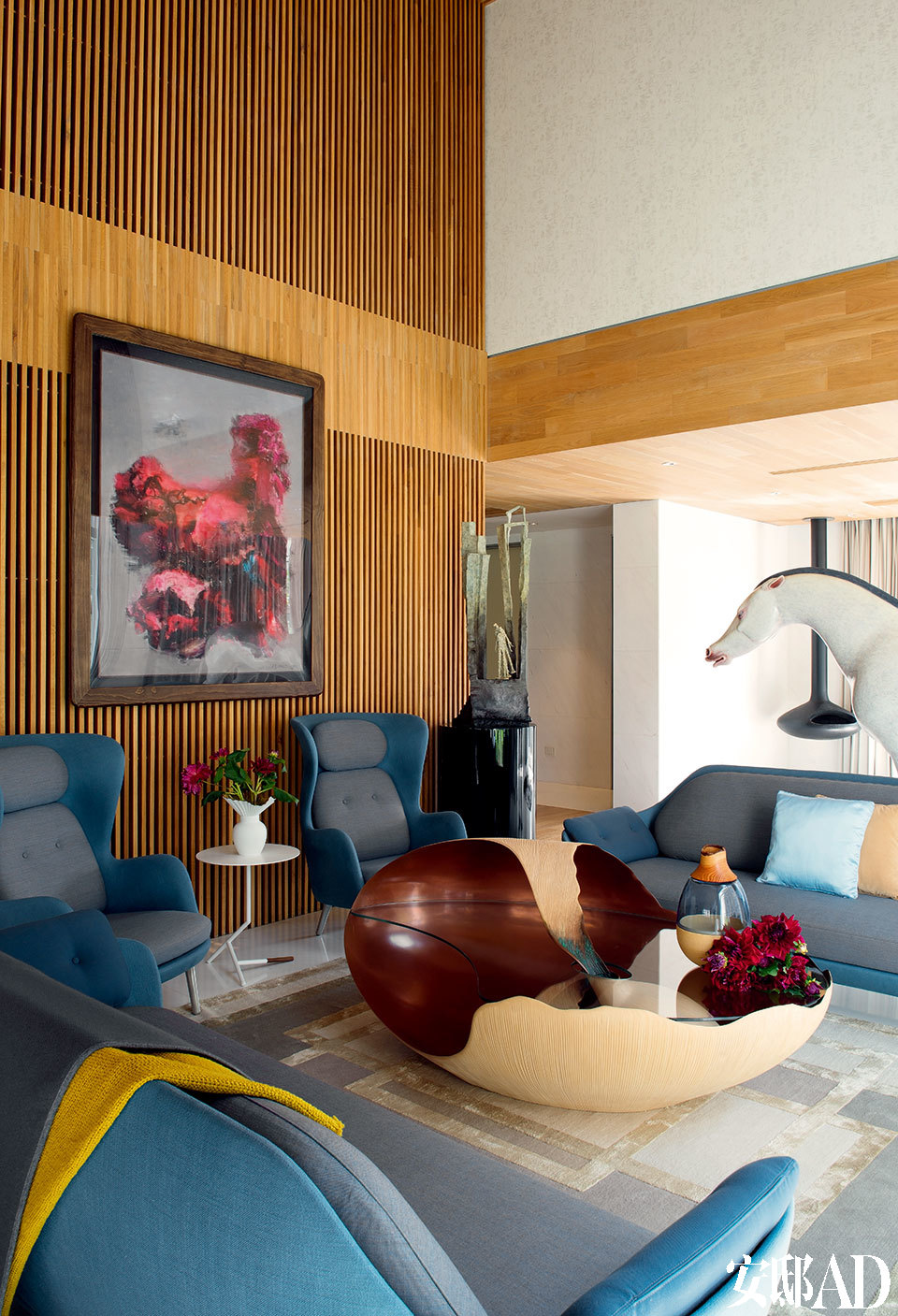 木格栅是贯穿整个家的主题，温暖着大空间，也调节着小视线。客厅的沙发区，沙发与两只扶手椅均为Publicof Fritz Hansen品牌，购自设计共和，Mollusque艺术茶几由Marc Fish设计，在铸好的铜模上贴了上千片梧桐木皮制成。地毯来自The Rug Company，木格栅上的画作是周春芽的“石头”系列，创作于1999年。画作右侧的青铜雕塑来自法国女艺术家瓦儿（Val），画作下方的白色茶几由Brad Ascalon设计，同样来自Ligne Roset写意空间。