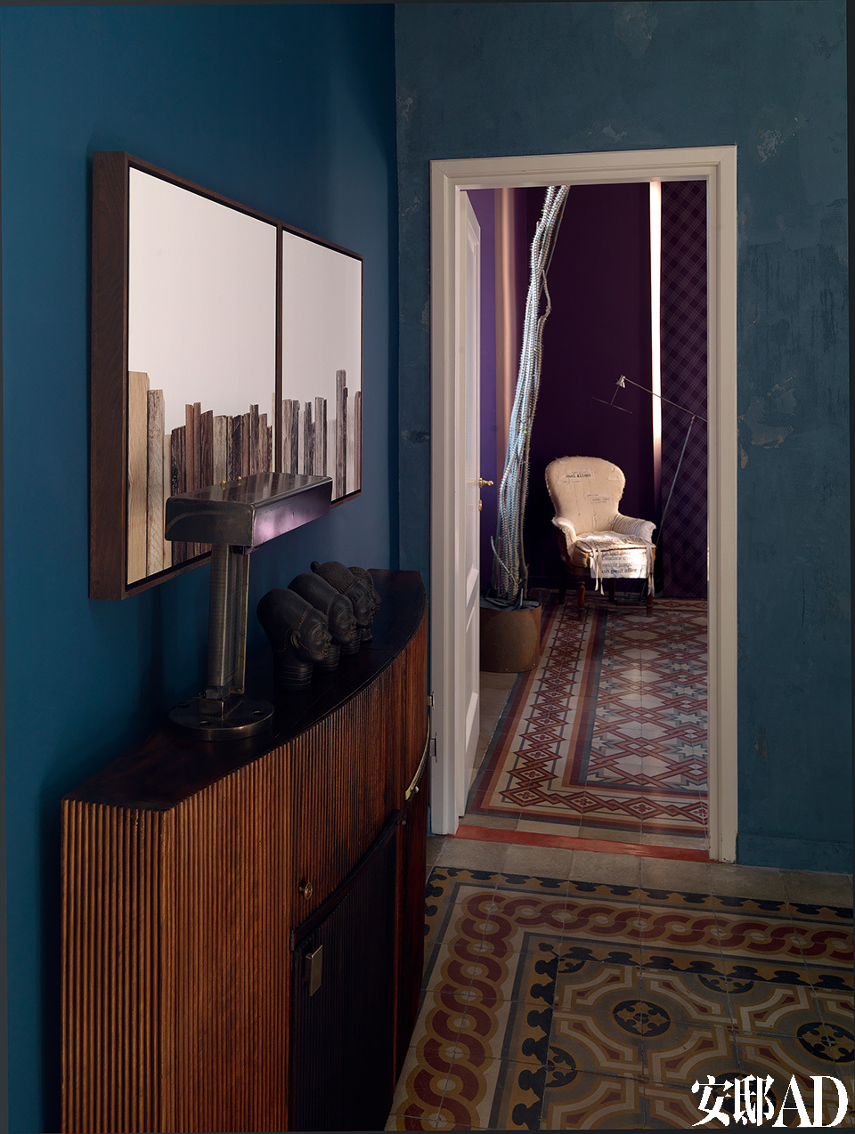 从客厅向卧室望去，质朴的地砖起到了非常关键的衔接作用，它也为墙面的用色提供了灵感。客厅木制抽屉柜上方的艺术品是由 Lorenzo Butti创作的，而柜子上摆放的台灯是Ugo Ambroggio的作品。