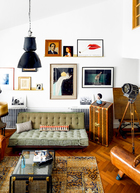 沙发背后的墙面，由多幅小尺寸画作组成，两个贴墙固定的金属小架，真是布置小尺幅画作的好主意！客厅中的黑色吊灯，是从荷兰淘到的古董工业灯。墙面上方第一排的3幅作品，分别是韦晴早年在巴黎拍卖买到的老油画、季鑫2015年的作品《点绛唇》，以及Tom Wesselmann于1967年在美国达拉斯美术馆个展的老海报。